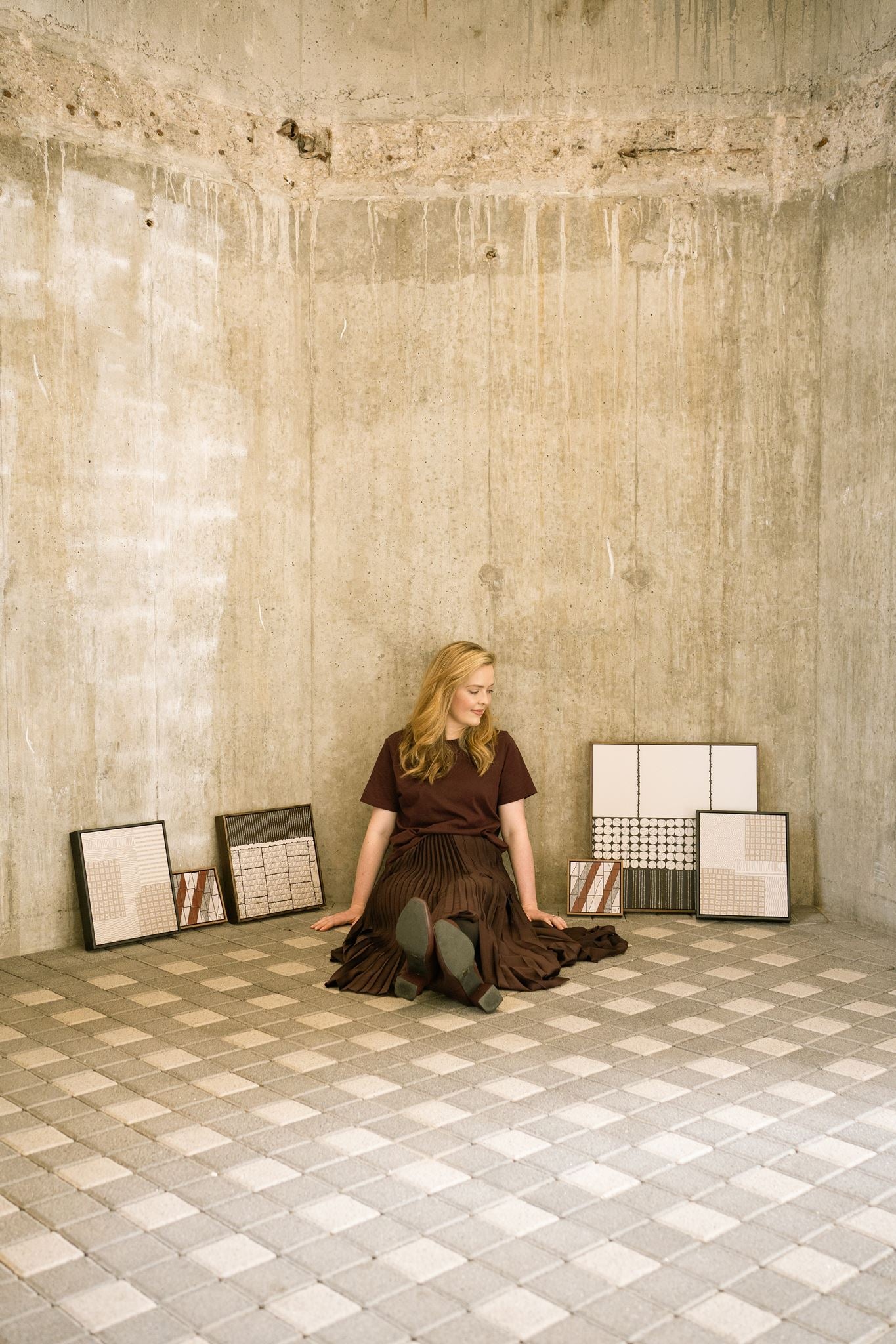 Visual artist Anna Mills surrounded by a collection of handcrafted contemporary abstract polymer clay artworks in an architectural concrete space.
