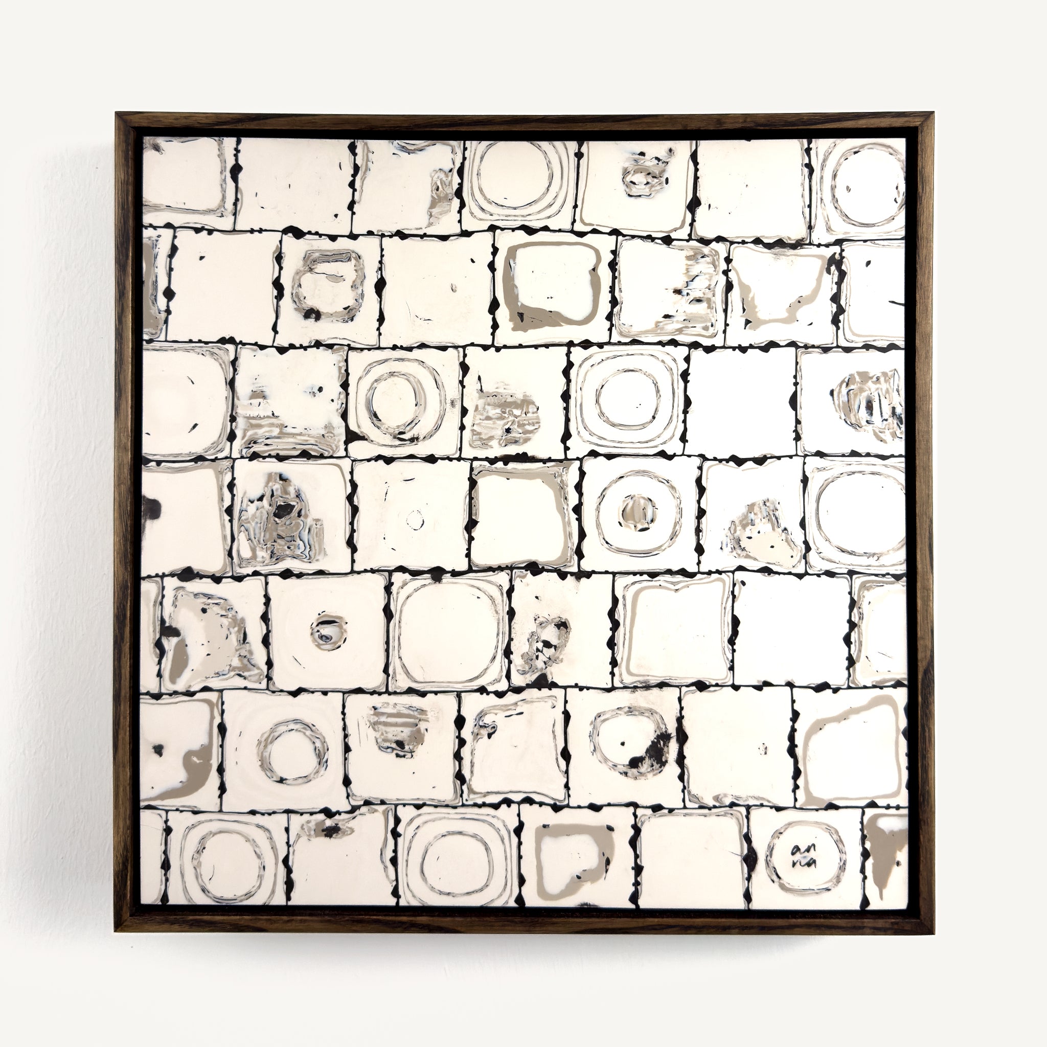 Ēa (Study II), a contemporary abstract polymer clay artwork, by Anna Mills, composed of a grid of individually hand-cut cane tiles, each revealing unique concentric patterns created from layered clay. Soft ivory, warm grey and dark brown/black tones evoke geological formations and topographic contours, while the irregular tile edges and subtle surface variations celebrate the handmade process. Presented in a solid wood tray frame finished in dark English walnut.