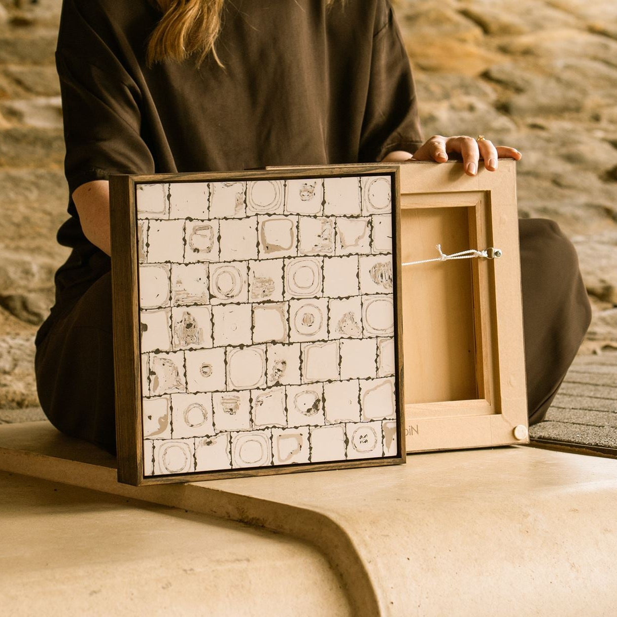 Artist Anna Mills sat with framed contemporary abstract polymer clay artwork shown from the front and reverse, highlighting the stained wooden tray frame, hanging hardware and signed back panel.
