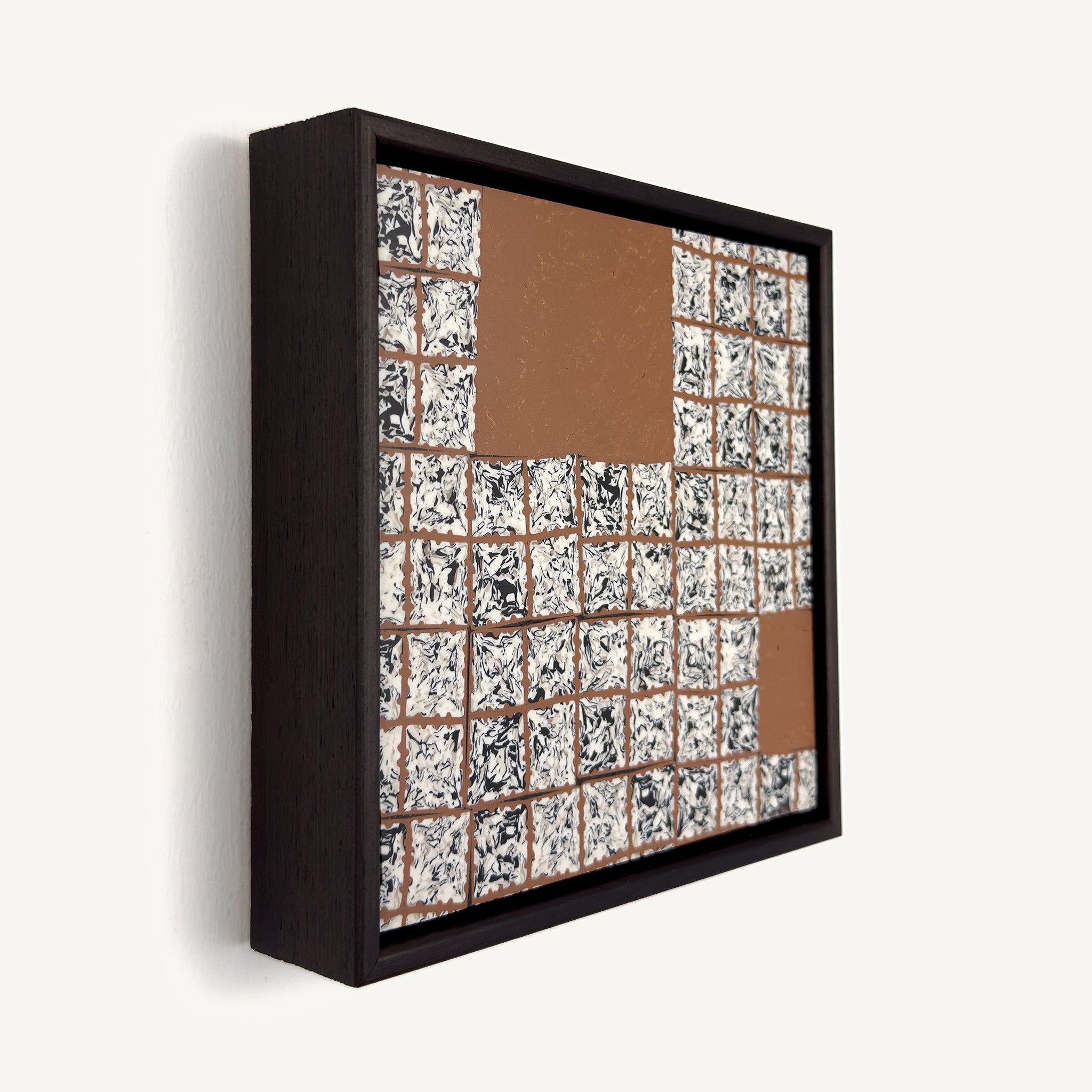 Greót I, at an angle, a contemporary abstract polymer clay artwork featuring a grid of individually sliced black, white and beige patterned squares arranged around open terracotta-coloured negative spaces. The composition is presented in a solid wood veneer tray frame finished in dark English walnut, measuring 17 × 17 cm.