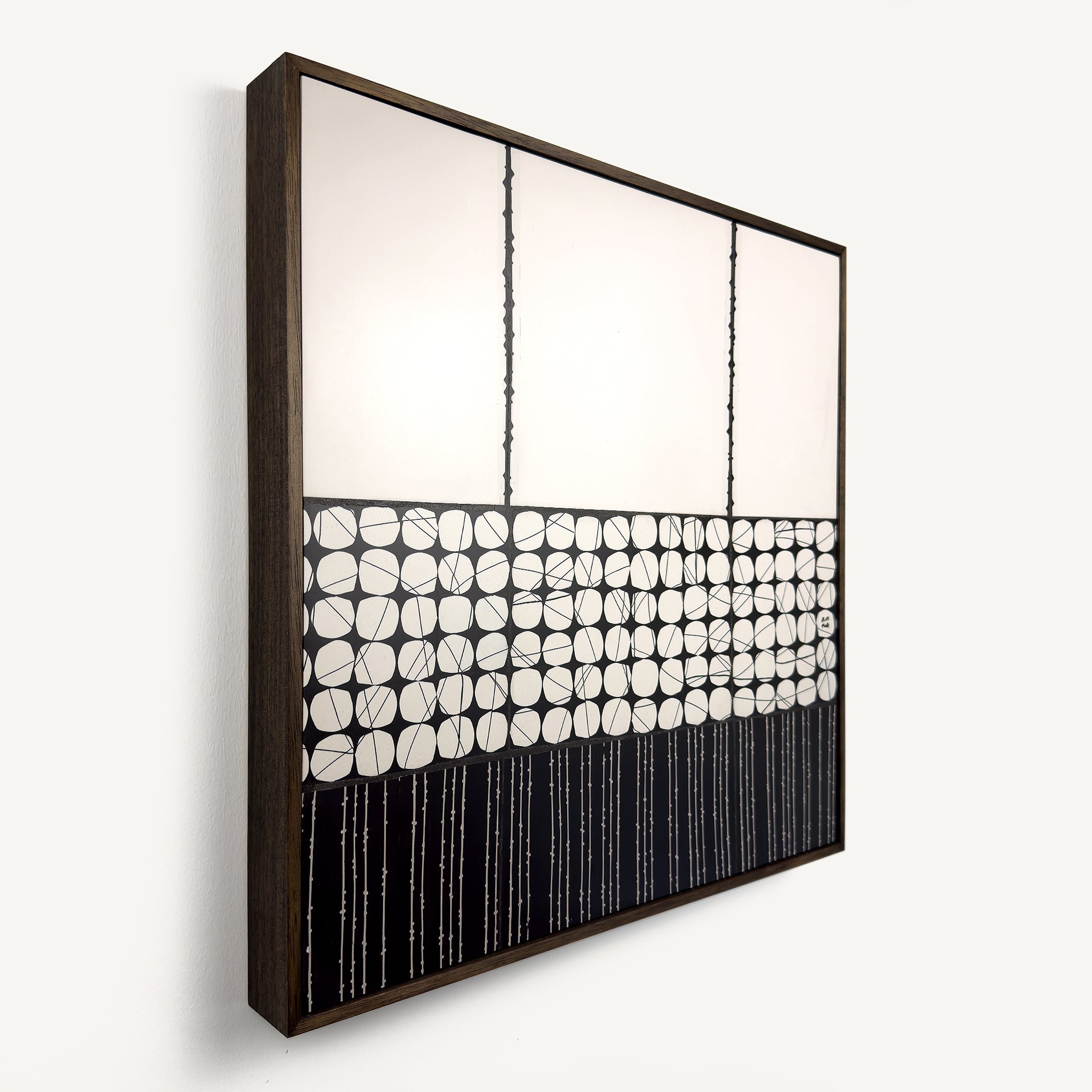 Heġe, a contemporary abstract polymer clay artwork measuring 52 × 52 cm, by artist Anna Mills. A minimalist composition combines a spacious off-white upper field with a central band of hand-cut organic geometric forms outlined by fine black lines, anchored by a bold black section of delicate vertical linework below. Subtle handcrafted textures and irregularities create a quiet balance between structure and organic movement. Presented in a solid wood tray frame finished in dark English walnut.