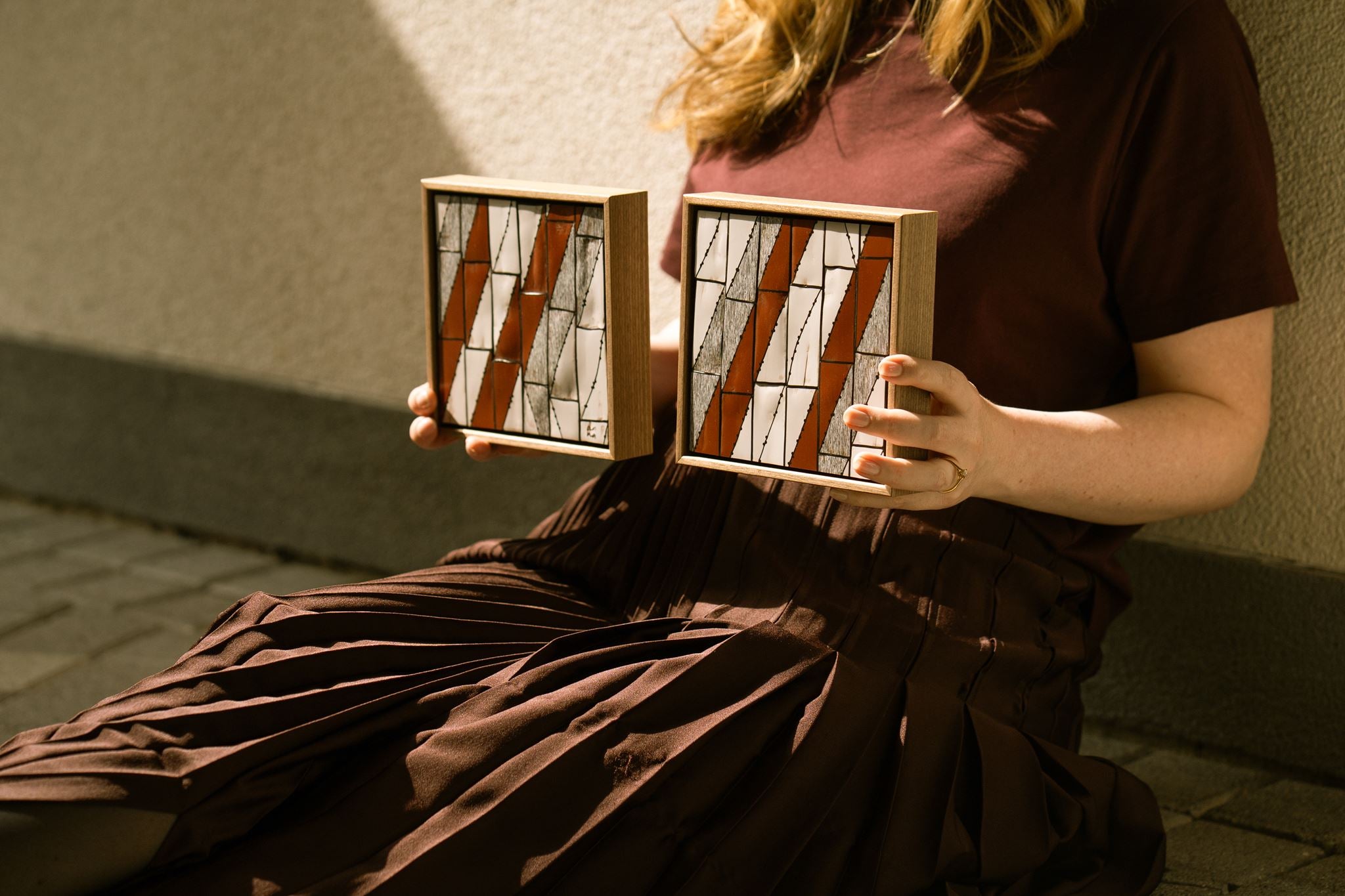 Rād I and Rād II, two framed, small contemporary abstract polymer clay artworks featuring bold geometric patterns in cream, a charcoal mix and deep rust, shown held by the artist Anna Mills.