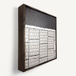 Steppe, a contemporary abstract polymer clay artwork measuring 32 × 32 cm, by artist Anna Mills. Photographed at an angle. A bold black upper section of fine vertical lines contrasts with a structured arrangement of hand-cut ivory geometric tiles below, each marked with delicate linear details. Irregular edges, subtle surface variations and visible handcrafted textures create a quiet balance between order and organic imperfection. Presented in a solid wood tray frame finished in dark English walnut.